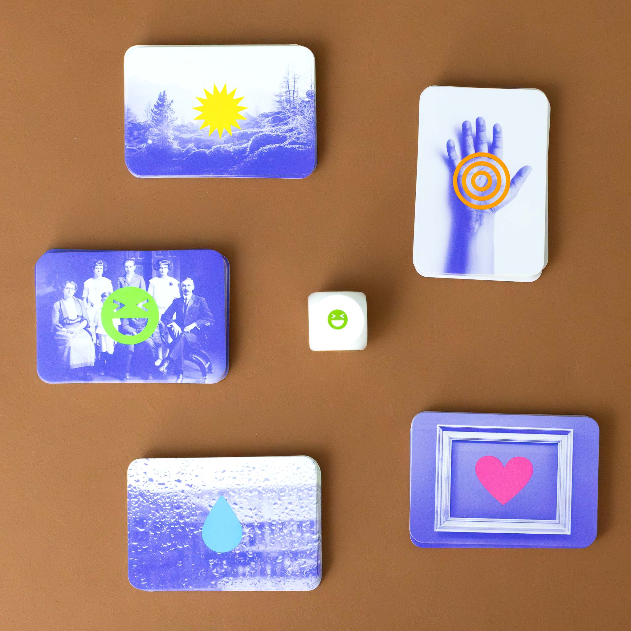 blue-images-on-cards-of-a-hand-with-orange-swirl-field-with-yellow-sunburst-family-portrait-with-green-smiley-face-rain-on-window-with-blue-drop-and-frame-with-pink-heart-white-die-with-green-smiley-face