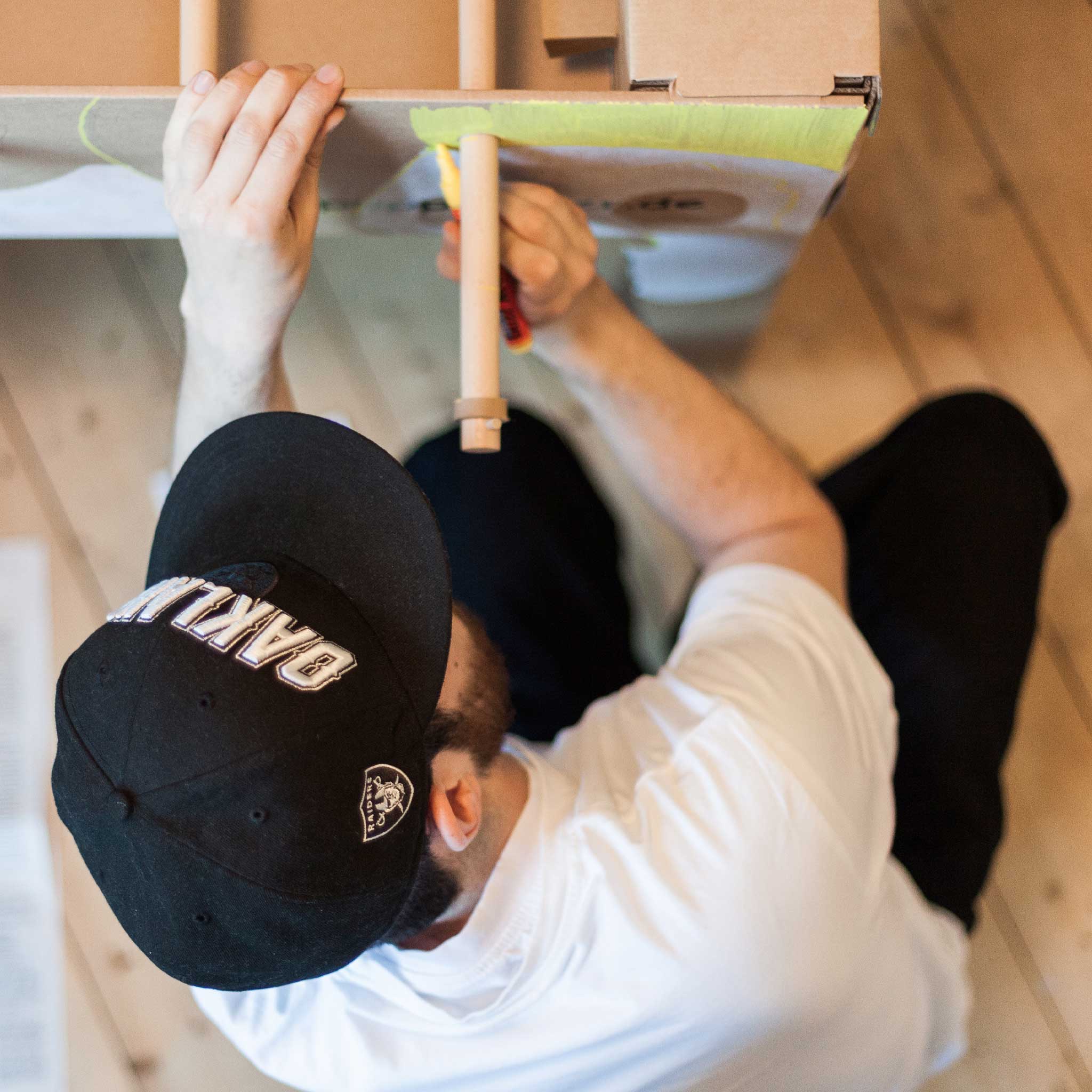 cardboard-foosball-table-side-view-of-adult-with-a-black-snapback-hat-coloring-in-the-side-of-the-table-in-yellow